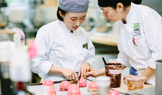 A 草榴短视频baking instructor and student look over pink pastries